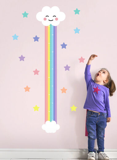 My Nametags rainbow cloud height chart op een roze muur met een klein meisje ernaast