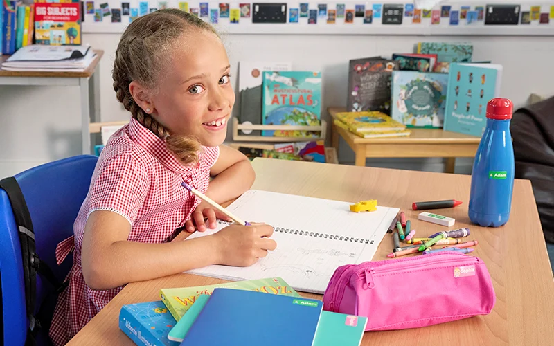 Girl at a classroom desk with a labelled water bottle, notebooks and pencil case